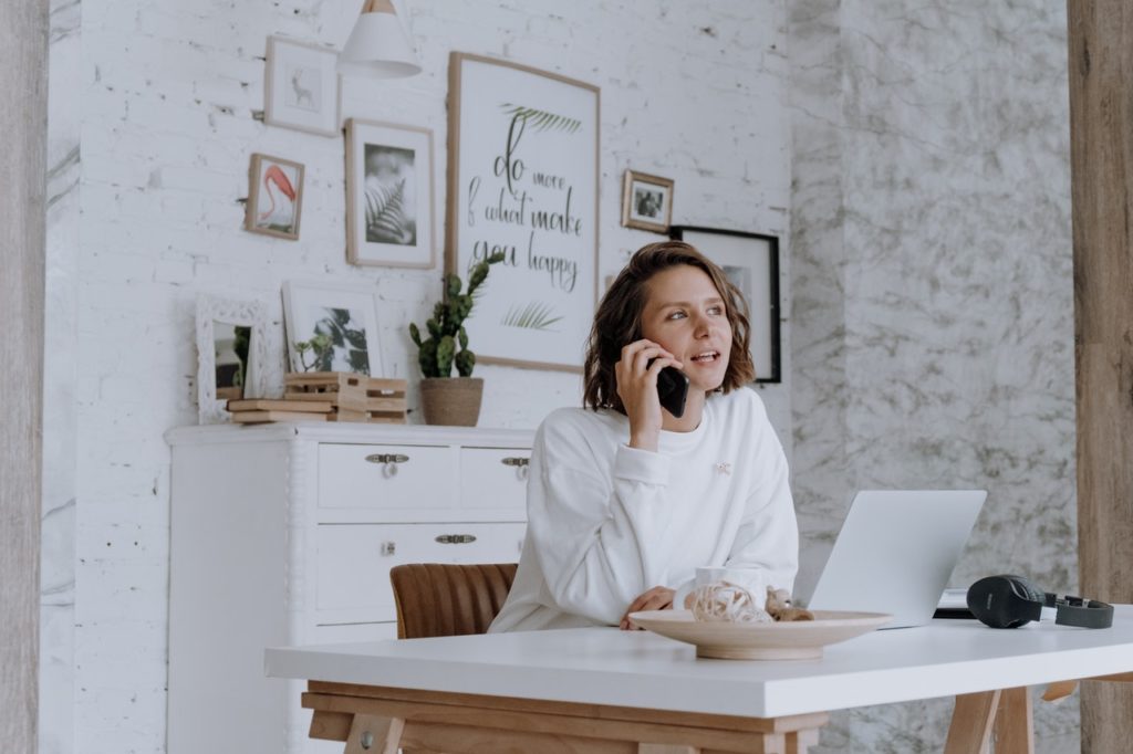 A woman on the phone looks at her laptop while searching for a home.